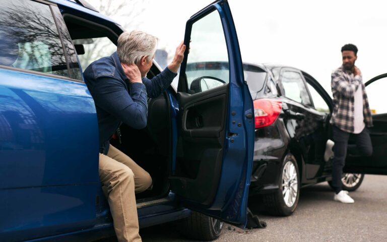 Driver and bystander inspecting a damaged vehicle after a car accident